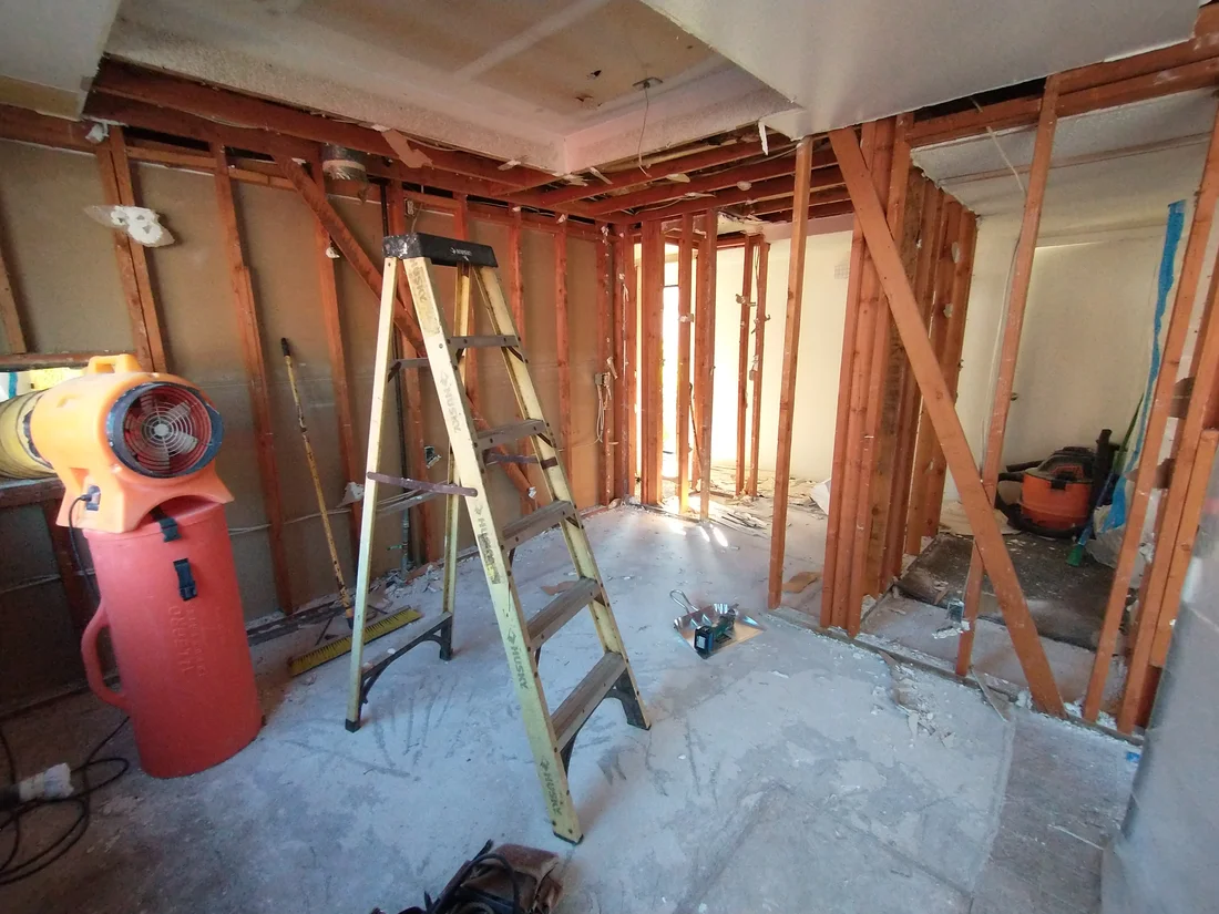 Kitchen demolition in progress with exposed wall framing and renovation equipment